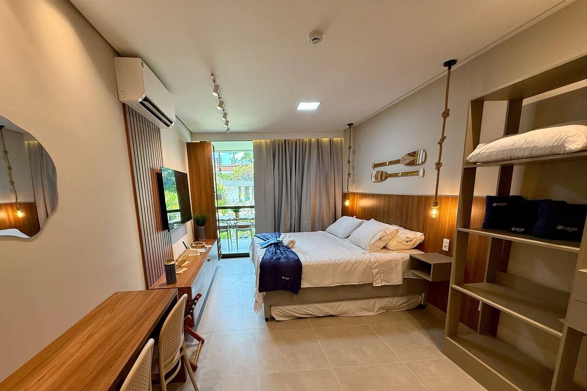 Ein Hotelzimmer mit Bett, Nachttischen, einem Schreibtisch, einem Spiegel und Blick ins Freie.