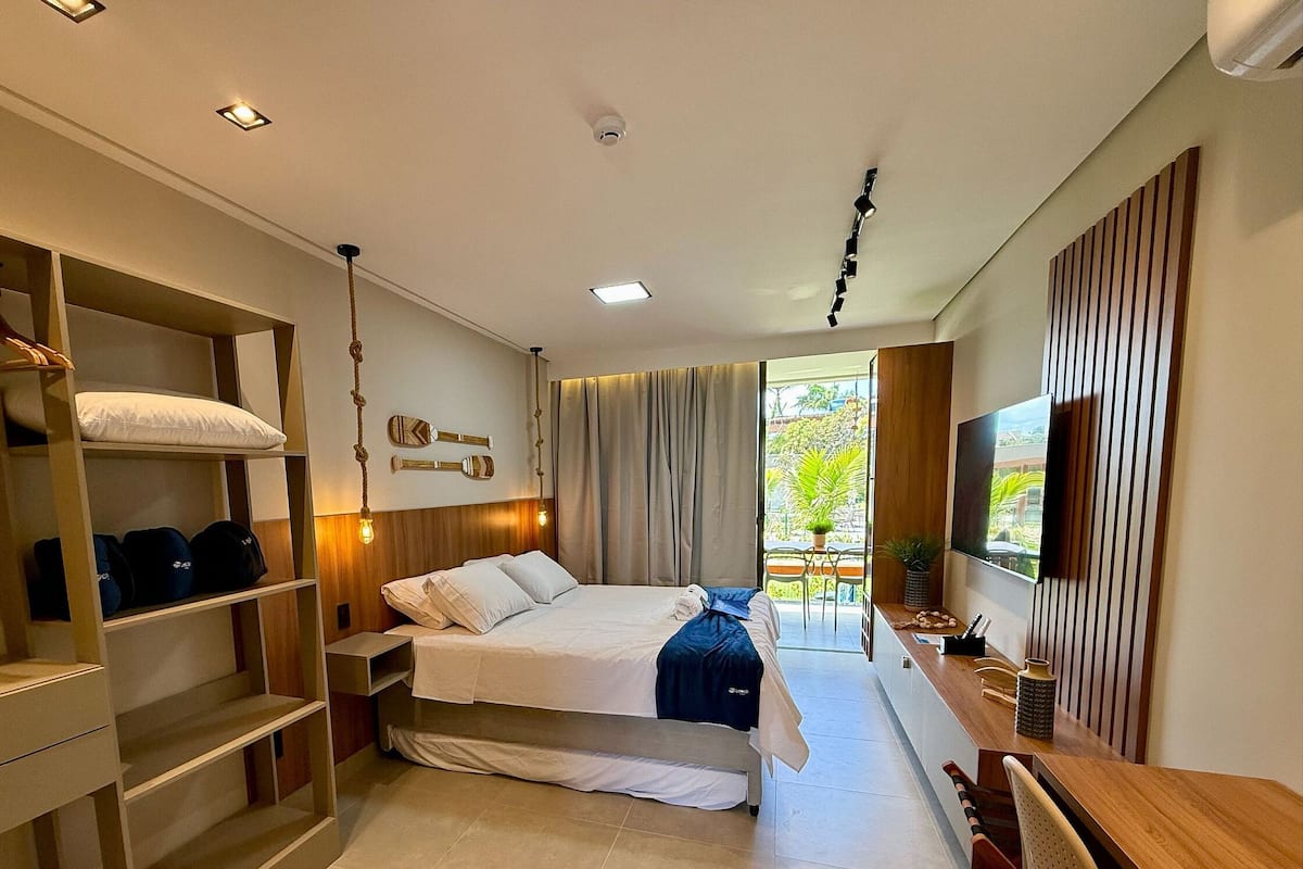 Ein modernes Hotelzimmer mit Bett, integriertem Kleiderschrank, Nachttisch und Fernseher.