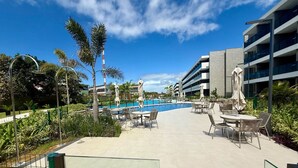 Zwembad van een resort met ligbedden en parasols, omringd door palmbomen en moderne gebouwen.