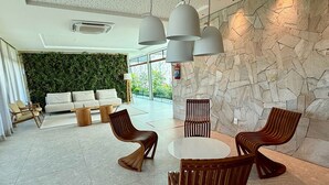 Een moderne lobby met een stenen muur, een groene wand, een bank, houten stoelen en hanglampen.