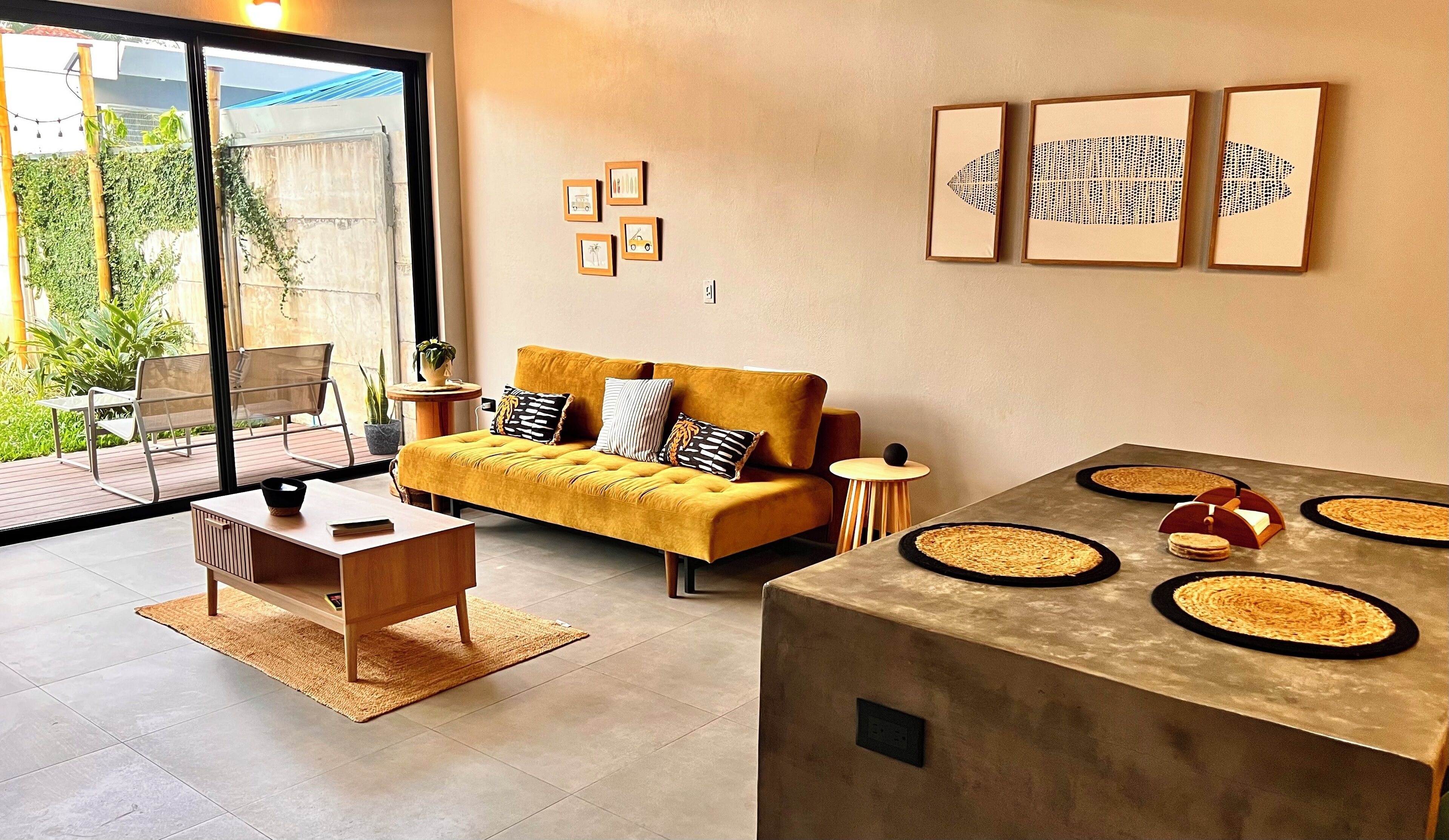 Een moderne woonkamer met een gele bank, een salontafel en een eethoek met geweven placemats.