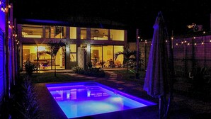 Una casa moderna amb piscina, finestres grans i mobiliari per a l'exterior.