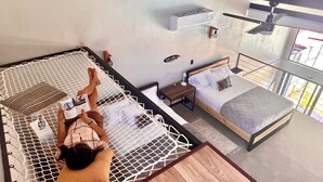Una habitació amb un llit hamaca, un llit de fusta, una taula petita i un ventilador de sostre.