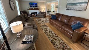 A living room with a brown leather sofa, a round coffee table, and a flat-screen TV mounted above a fireplace.