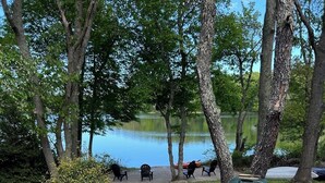 An outdoor seating area with Adirondack chairs, a fire pit, and a view of a lake.