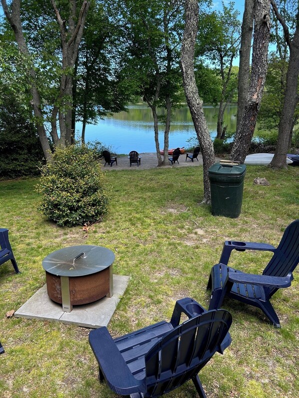 An outdoor seating area with Adirondack chairs, a fire pit, and a view of a lake.