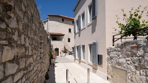 A narrow street with stone walls and buildings with shutters.