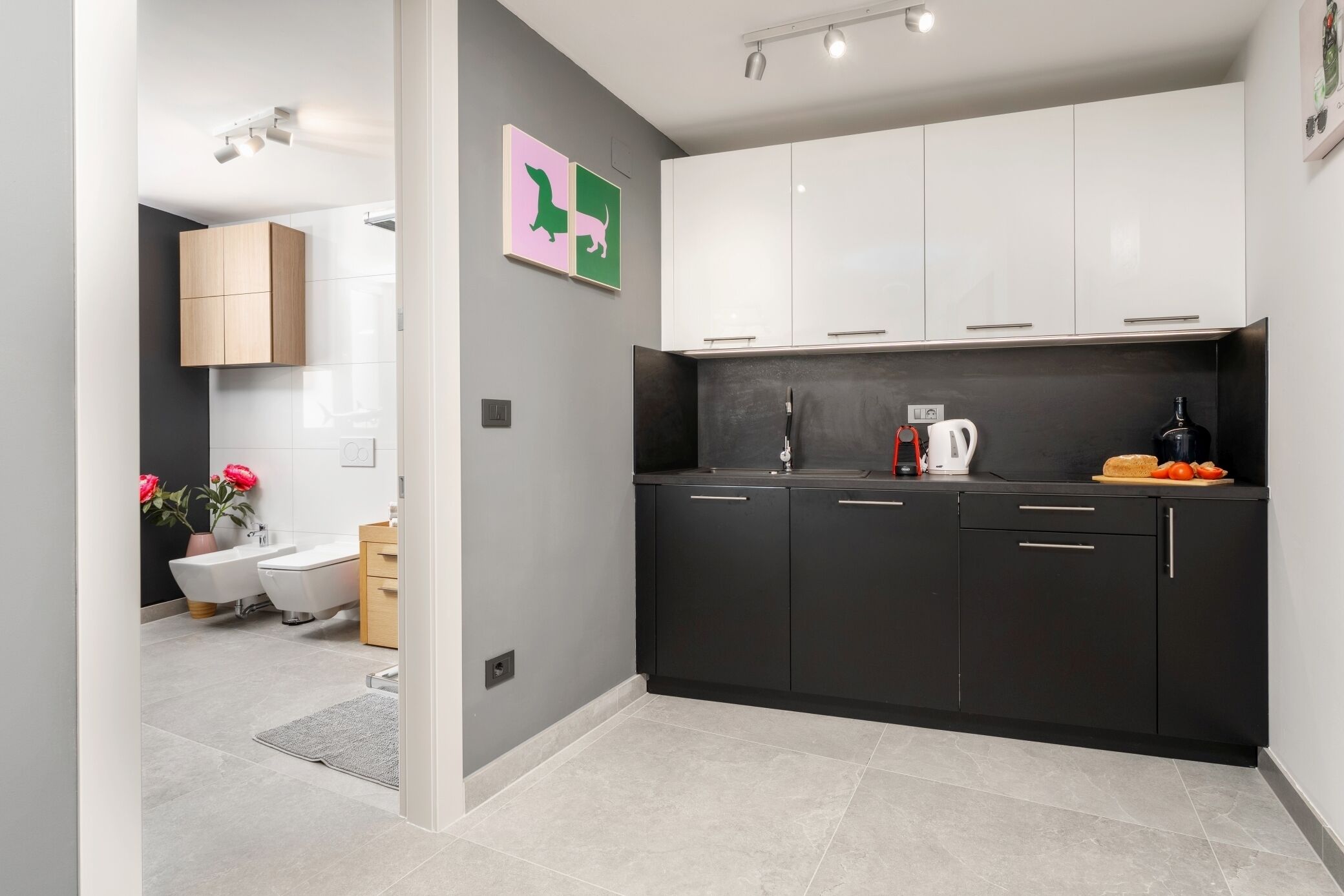 Eine moderne Küche mit schwarzen Schränken, einer weißen Arbeitsplatte und einem Spülbecken. Auf der Arbeitsplatte stehen eine Kaffeemaschine und ein Wasserkocher.