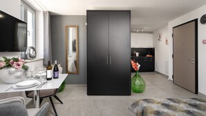 A modern living room with a dining area, a black wardrobe, a green vase with flowers, and a kitchen in the background.
