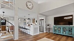 Ein geräumiges Wohnzimmer mit Holzboden, einer großen Uhr, einem türkisblauen Schrank und einer Treppe zu einer anderen Ebene.