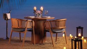 Una mesa con sillas, velas y un farol bajo una palmera al anochecer.