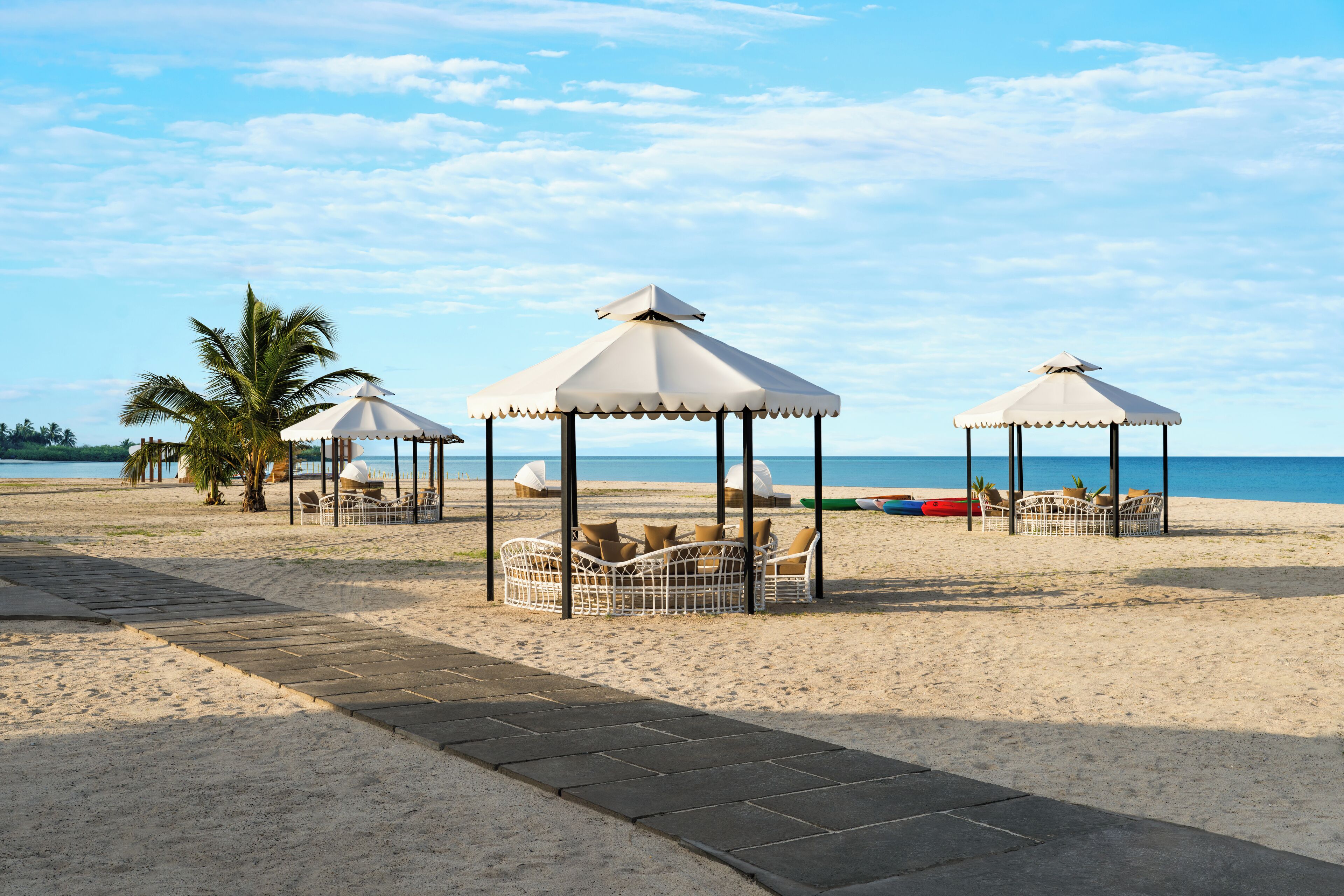A beach with three white gazebos, palm trees, and lounge chairs.