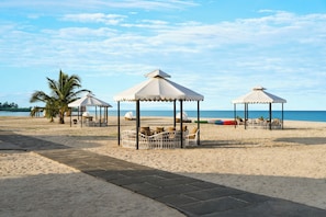 A beach with three white gazebos, palm trees, and lounge chairs.