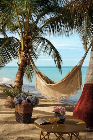 Escena de playa con una hamaca, una mesa con bebidas y flores, y una cesta de flores.