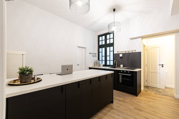 A modern kitchen with a large island, dark cabinetry, and a black stove.