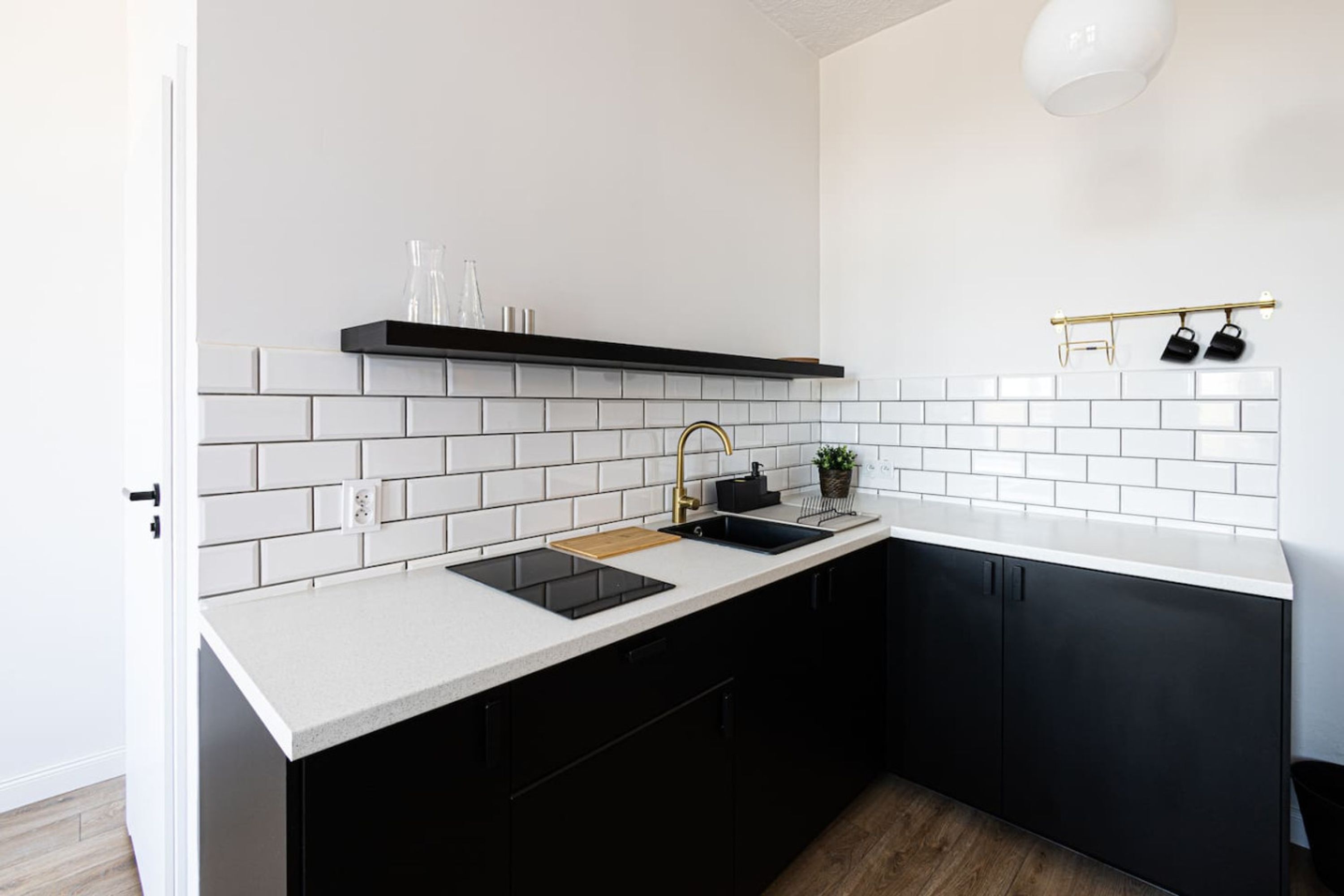 Cocina moderna con azulejos blancos tipo metro, gabinetes negros, encimera negra, grifo dorado y salpicadero negro.