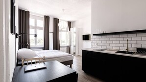 A modern bedroom with a bed, bedside table, and a desk with a laptop. There is a kitchen area with a sink and a TV mounted on the wall. - Verde 1 Studio z Kuchni Wifi Dolny Gda sk (Gdansk)