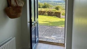 A hallway leading to a door with a view of a grassy landscape and distant hills.