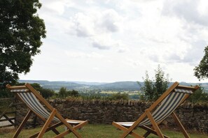 Two wooden lounge chairs with striped cushions, positioned on a grassy area with a stone wall behind them, overlooking a scenic landscape. - Belmont House (Cappoquin)