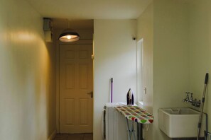 A narrow hallway with a door, a radiator, an ironing board, and a sink. - Belmont House (Cappoquin)
