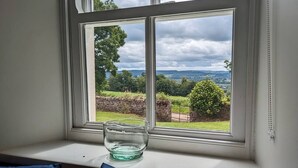 A window seat with a clear view of a rural landscape, including trees and a stone wall.