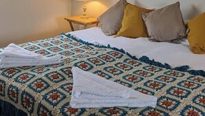 A neatly made bed with a patterned blanket and pillows, a bedside lamp, and a small table.