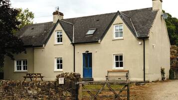 A two-story house with a blue door, a stone wall, and a wooden gate.