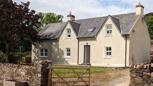 A two-story house with a stone wall entrance, a gravel driveway, and a small garden area.