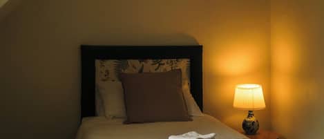 Una habitación de hotel con una cama, una mesita de noche con una lámpara y una ventana.