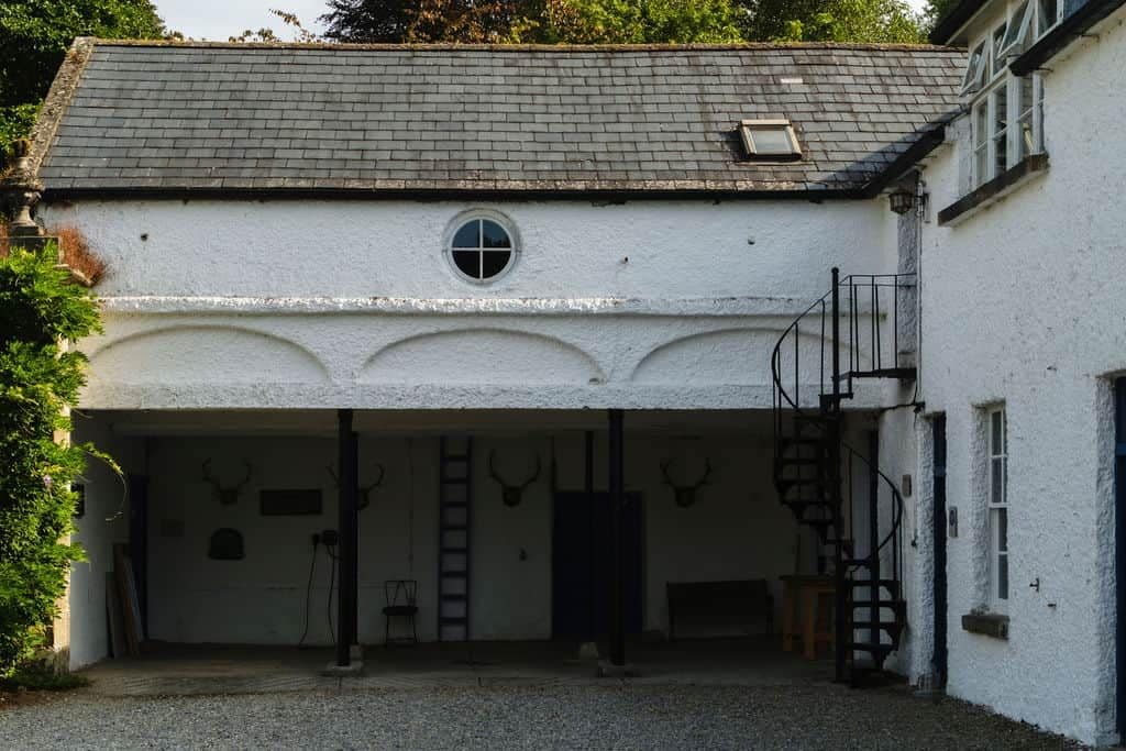 A white building with a covered entrance, a spiral staircase, and a small window.