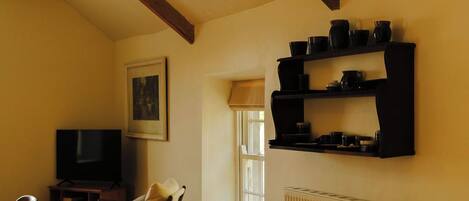 A living room with a television, a chair, a window, and a shelf with black items.