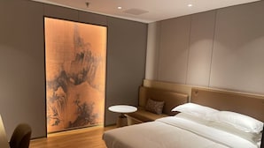 A modern hotel room with a large bed, a small round table, and a wall-mounted artwork.