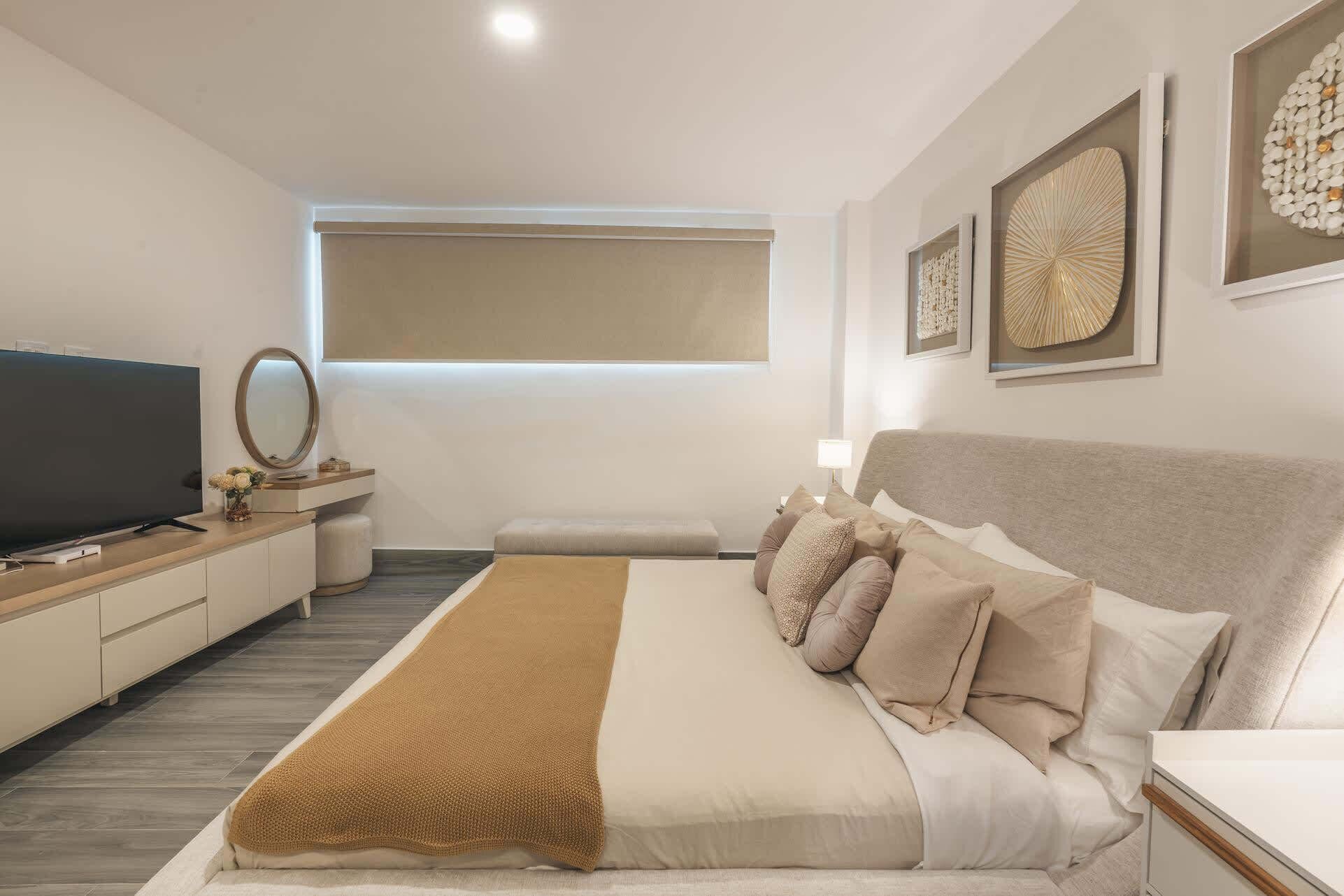 Quarto moderno com uma cama grande, televisão, mesa de cabeceira e janela com persianas.
