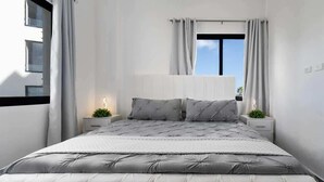 Un dormitorio moderno con una cama grande, paredes blancas y una ventana con cortinas.