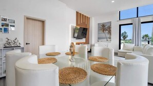 Una sala moderna con una mesa de centro de vidrio, sofás blancos y individuales tejidos.