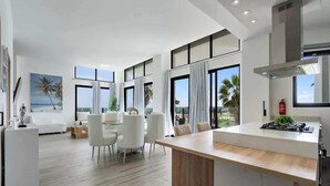 Una cocina moderna con una isla central, ventanas amplias y un comedor con sillas blancas.