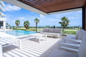 Ein moderner Poolbereich im Freien mit einem weißen Pool, Liegestühlen und Blick auf den Ozean und Palmen.