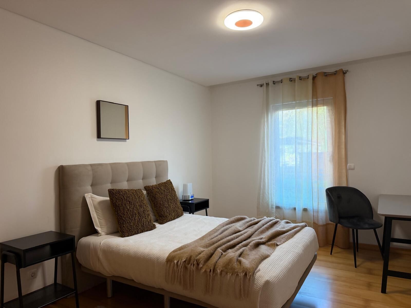A bedroom with a bed, bedside tables, a chair, a desk, and a window with curtains.