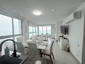 A modern kitchen with a dining area, large windows, and a TV on the wall.