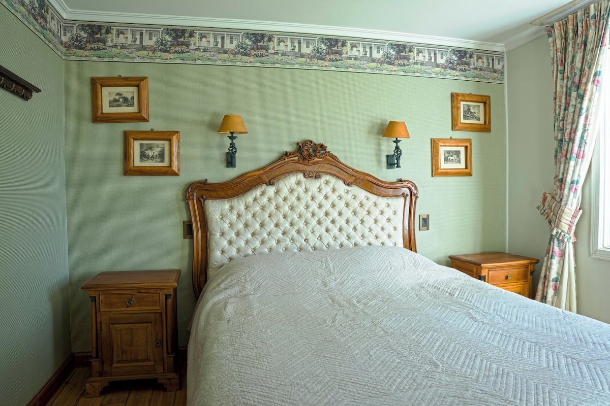 Ein Schlafzimmer mit einer gesteppten Kopfteil, einem Bett mit weißer Bettdecke, zwei Nachttischen und gerahmten Bildern an der Wand.