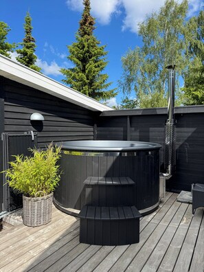 A hot tub with a wooden deck, a potted plant, and a metal heater.