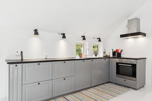 A modern kitchen with grey cabinets, a stainless steel oven, and pendant lights. - Newly renovated holiday home near the beach (Væggerløse)