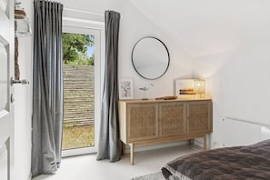 Ein Schlafzimmer mit einem großen Fenster, einem runden Spiegel, einem Holzschrank und einem Bett.