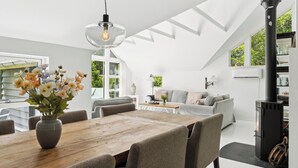 Un loft espacioso con una mesa de comedor de madera, sillas tapizadas de color gris, un sofá y un estufa de leña negra.