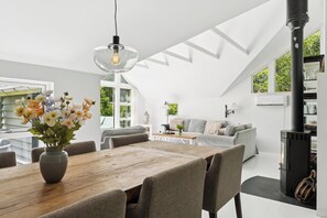 Ein geräumiger Loft mit einem Holzesstisch, grau gepolsterten Stühlen, einer Couch und einem schwarzen Kaminofen.
