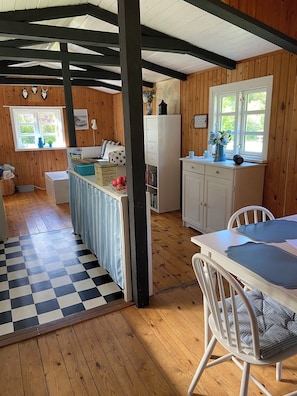 Et hyggeligt sommerhusindretning med et køkken, spiseområde og et ternet gulv.