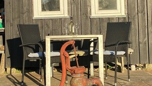 A rustic wooden shed with two windows, a metal roof, and two black chairs with cushions. - A cozy older summerhouse on a small island (Orø)