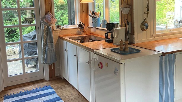 A kitchen with wooden walls, a large window, and a door leading outside. - A cozy older summerhouse on a small island (Orø)