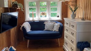 A cozy room with a blue sofa, wooden walls, a white dresser, and a TV. - A cozy older summerhouse on a small island (Orø)