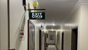 A hotel hallway with exit signs, fire extinguishers, and suit signs. - AŞKALE BİZİM OTEL (Askale)